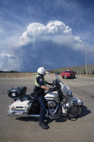 An Alberta Sheriff manning a roadblock on Highway 63 watches a massive plume of smoke over Fort McMurray Wednesday, May 4, 2016. (photograph by Chris Schwarz/Government of Alberta)
