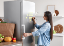 Woman writing a note on the fridge in a kitchen | Canva Pro